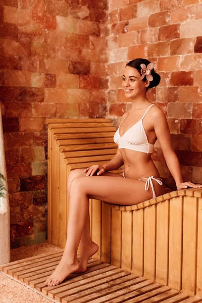 Jeune femme en bikini blanc sur banc en bois au centre spa — Photo de stock