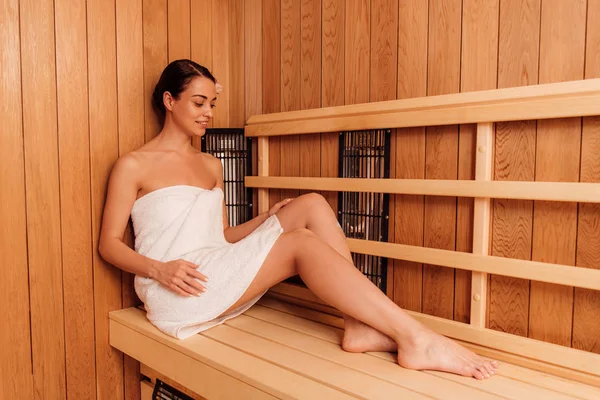 Femme souriante en serviette avec fleur dans les cheveux dans le sauna — Photo de stock