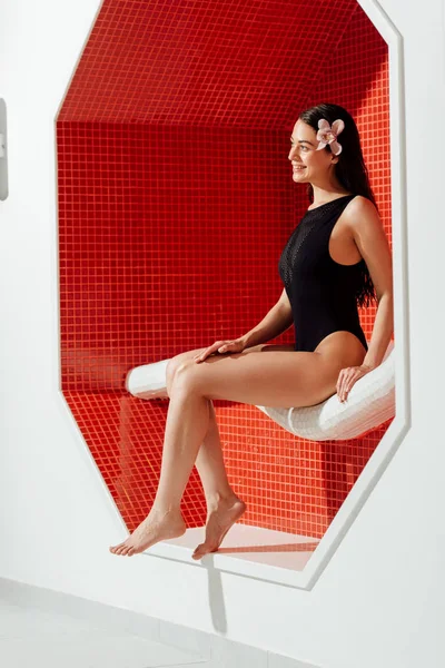 Jeune femme souriante en maillot de bain assis sur le canapé dans le centre de spa — Photo de stock