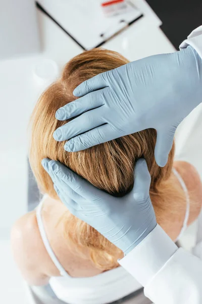 Vue aérienne du dermatologue en gants de latex examinant les cheveux du patient en clinique — Photo de stock