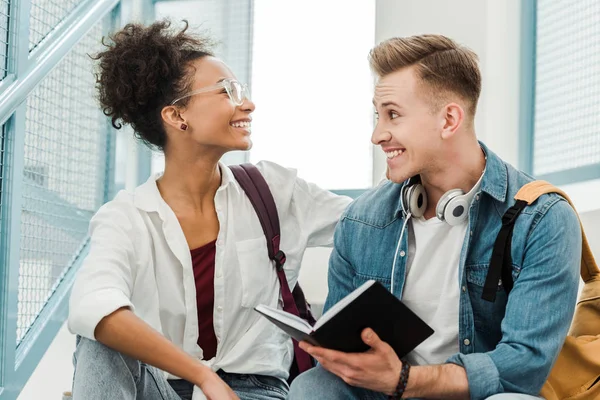 Two multiethinc students with notebook smiling in university — Stock Photo