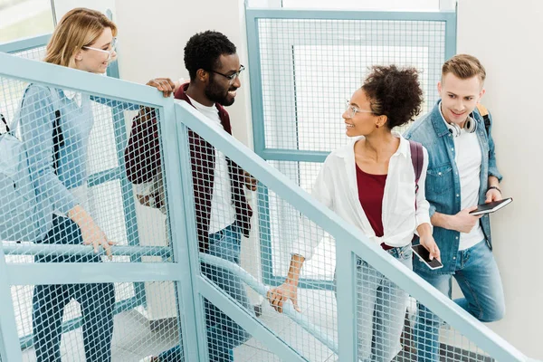 Four smiling multicultural students with backpacks on stairs in university — Stock Photo