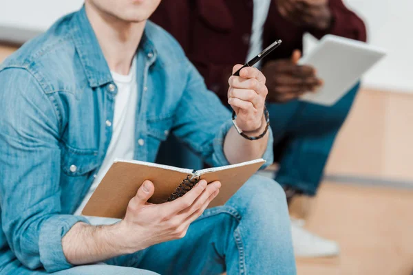 Vista parcial del estudiante en camisa de mezclilla con cuaderno y bolígrafo - foto de stock