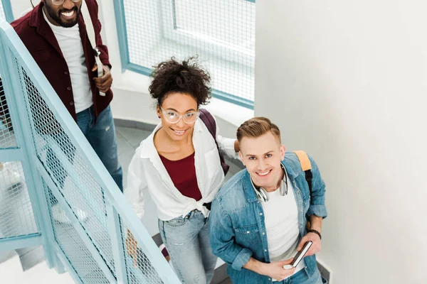 Overhead view of three smiling multiethnic students with backpacks — Stock Photo