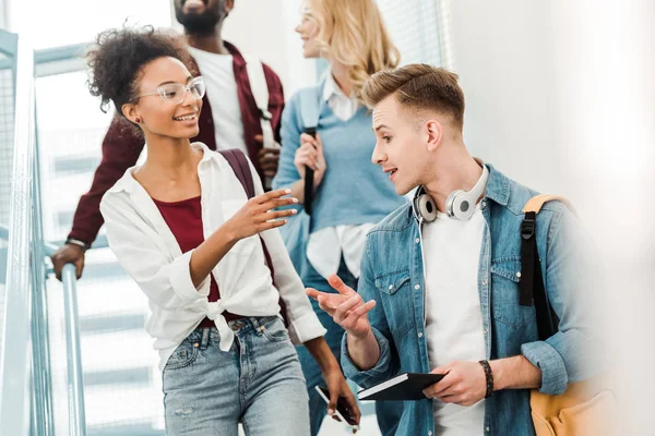 Vier lächelnde multiethnische Studenten mit Rucksäcken auf der Treppe — Stockfoto