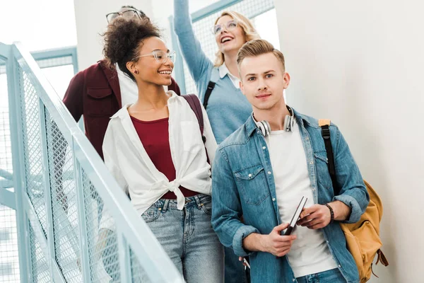 Quatro estudantes multiétnicos sorridentes com mochilas nas escadas — Fotografia de Stock