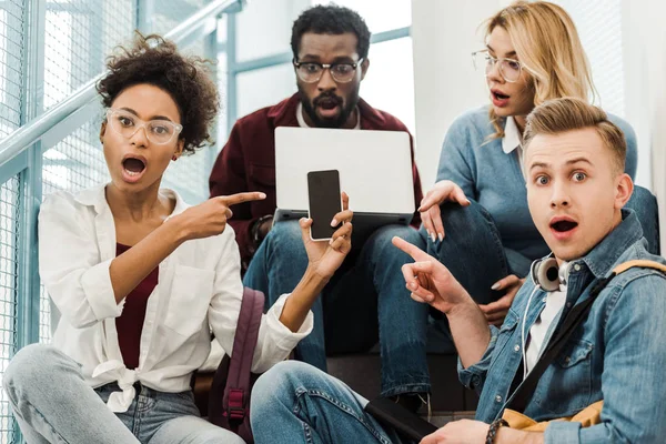 Group of shocked multicultural students with laptop and smartphone in university — Stock Photo