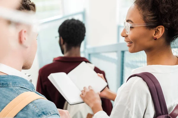 Enfoque selectivo en estudiantes multiculturales en gafas con cuaderno - foto de stock