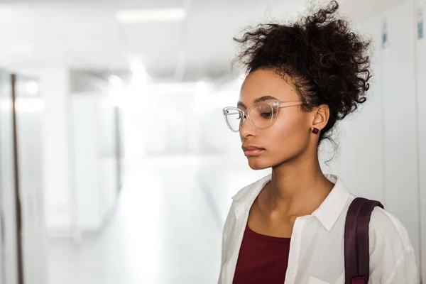Pensativo africano americano estudiante en gafas en pasillo - foto de stock