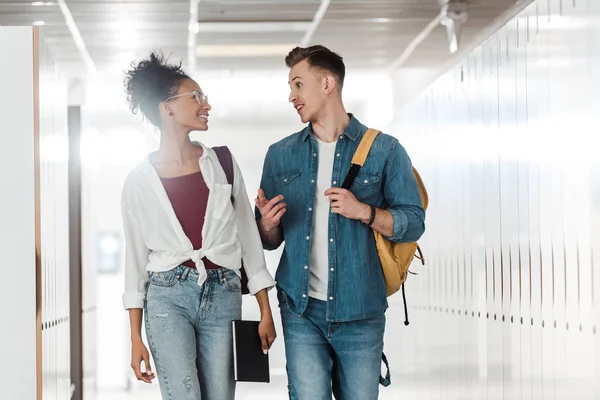 Two multiethnic students looking at each other in corridor in university — Stock Photo