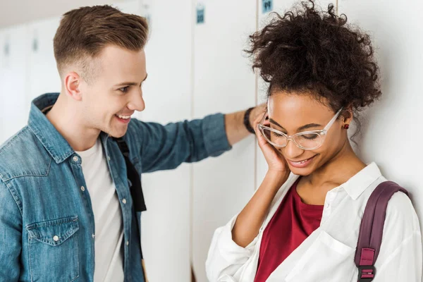 Smiling multiethnic students standing near lockers in university — Stock Photo