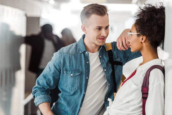 Smiling multiethnic students looking at each other in corridor in university — Stock Photo