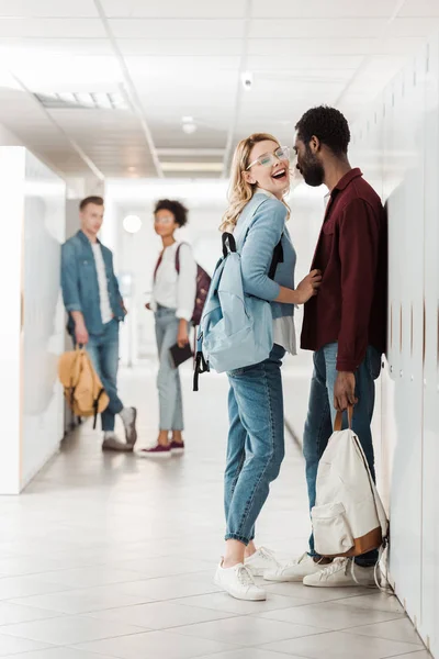 Vista completa de los estudiantes multiétnicos sonrientes de pie en el pasillo en la universidad - foto de stock