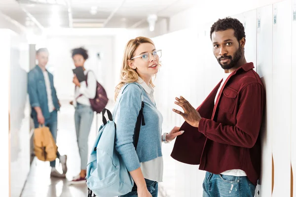 Smiling multiethnic students standing in corridor in college — Stock Photo