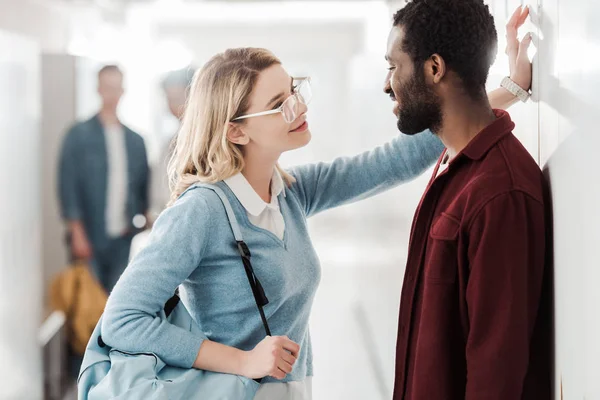 Lächelnde multiethnische Studenten, die auf dem Flur stehen und einander anschauen — Stockfoto