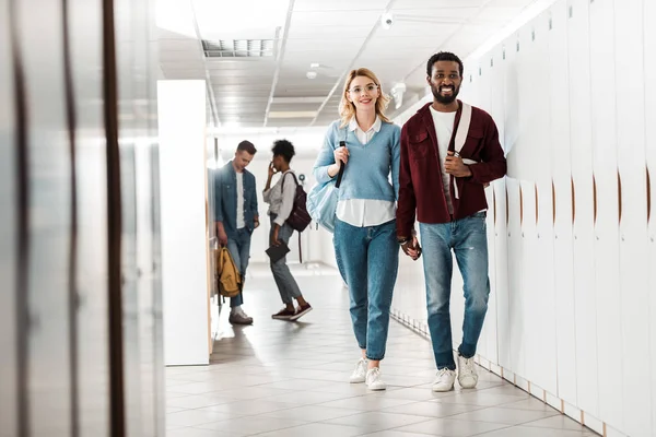 Ganzkörperansicht lächelnder multiethnischer Studenten, die sich im College an den Händen halten — Stockfoto