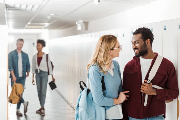 Smiling multiethnic students looking at each other in corridor in college — Stock Photo