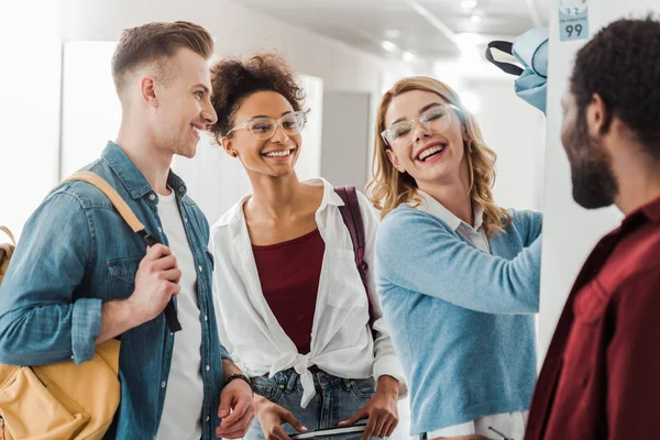 Quatro sorrindo estudantes multiétnicos em pé no corredor na faculdade — Fotografia de Stock