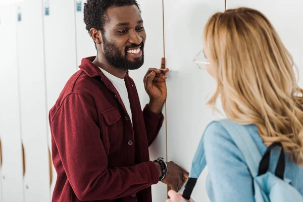 Zwei lächelnde multiethnische Studenten in der Nähe von Schließfächern im College — Stockfoto