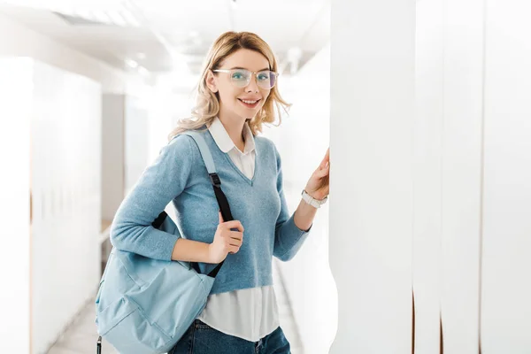 Smiling student in glasses with backpack opening locker in college — Stock Photo