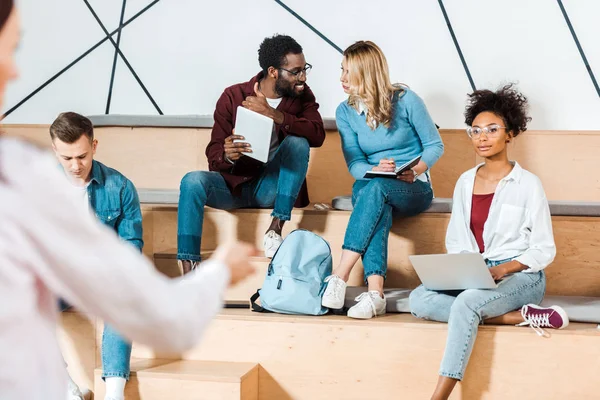 Multicultural students with laptop and digital tablet listening teacher in lecture hall — Stock Photo