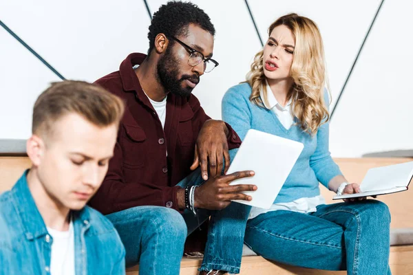 Tre studenti multiculturali con tablet digitale e taccuino in aula — Foto stock