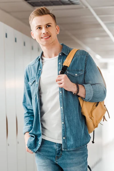 Étudiant souriant avec sac à dos regardant loin dans le couloir à l'université — Photo de stock