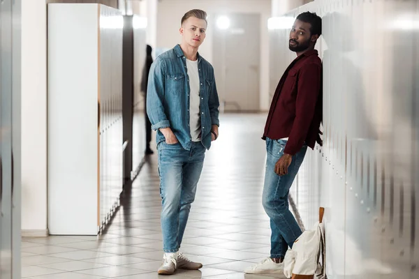 Vue complète de deux étudiants multiculturels près des casiers dans le couloir — Photo de stock