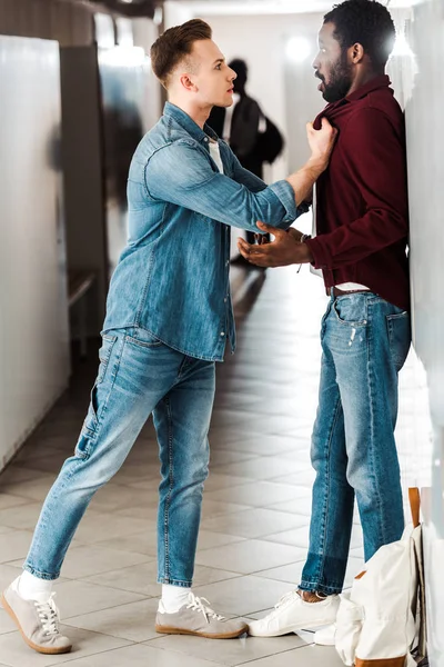 Vista completa de dos estudiantes multiculturales peleando en el pasillo en la universidad - foto de stock