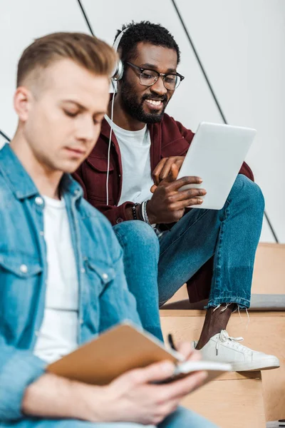 Sorrindo estudante afro-americano usando tablet digital e ouvir música em fones de ouvido — Fotografia de Stock