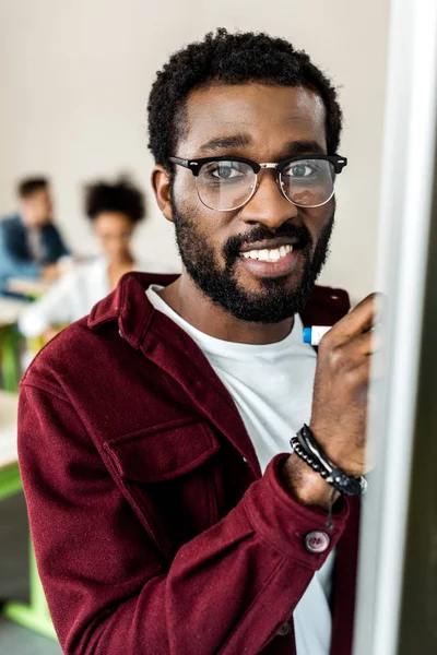 Sorrindo estudante afro-americano em óculos escrevendo no flipchart — Fotografia de Stock