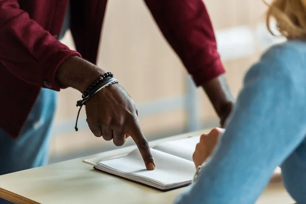 Vue partielle d'un étudiant afro-américain pointant du doigt un cahier — Photo de stock