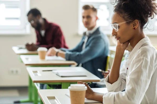 Multicultural students at desks writing during lecture in college — Stock Photo