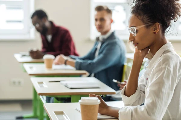 Étudiants multiculturels aux bureaux écrivant pendant la conférence au collège — Photo de stock