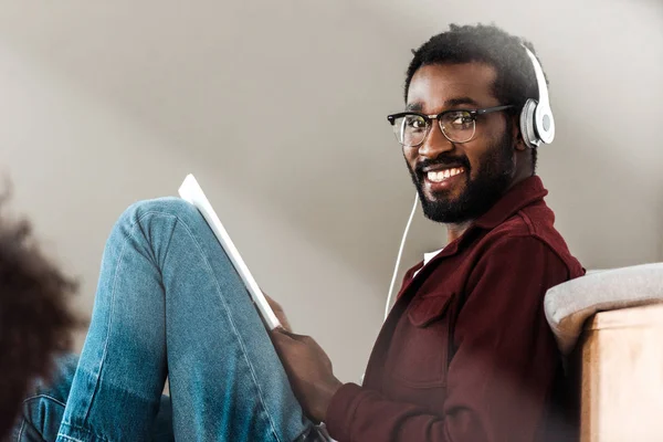 African american student in headphones using digital tablet in university — Stock Photo