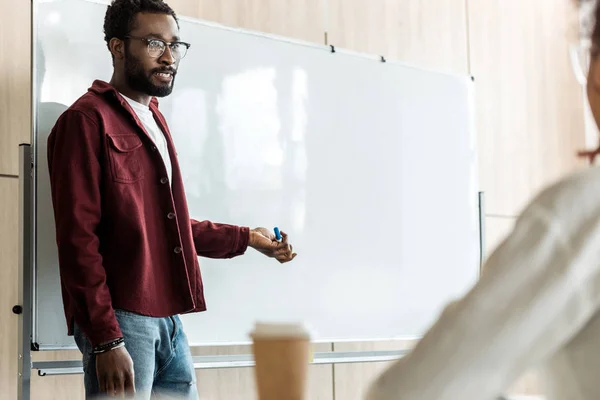 Étudiant afro-américain dans des lunettes debout près de tableau à feuilles — Photo de stock