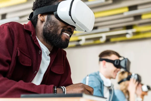 Selective focus of smiling multicultural students using vr headsets — Stock Photo