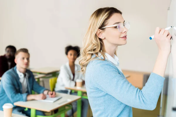 Graziosa studentessa in occhiali che scrive su flipchart con sorriso — Foto stock