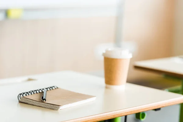 Selective focus of paper cup of coffee and notebook with pen on desk — Stock Photo