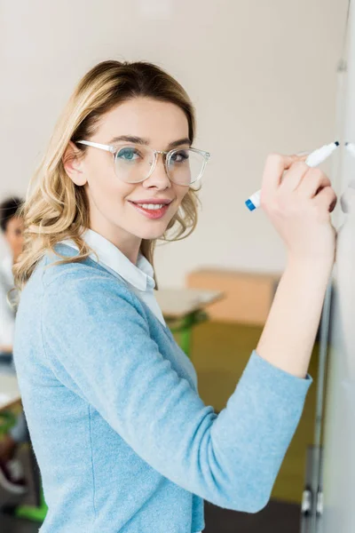 Pretty student in glasses writing on flipchart with smile — Stock Photo