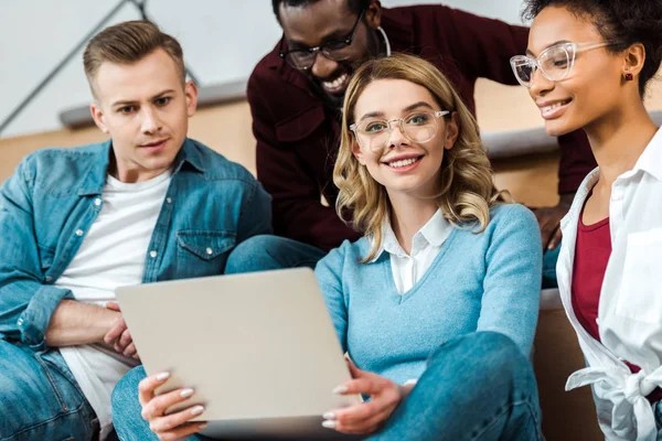 Smiling multicultural students with laptop in lecture hall — Stock Photo