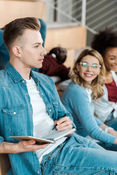 Estudiante con cuaderno sentado con amigos en la sala de conferencias - foto de stock