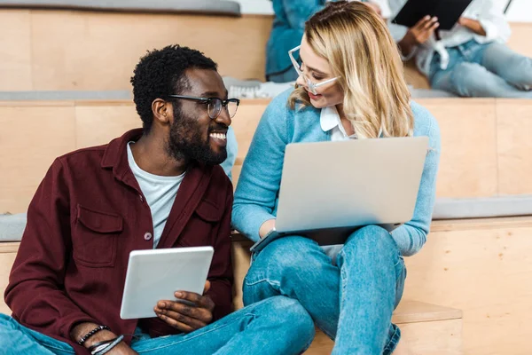 Estudiantes multiculturales sonrientes utilizando tableta digital y portátil en la sala de conferencias - foto de stock