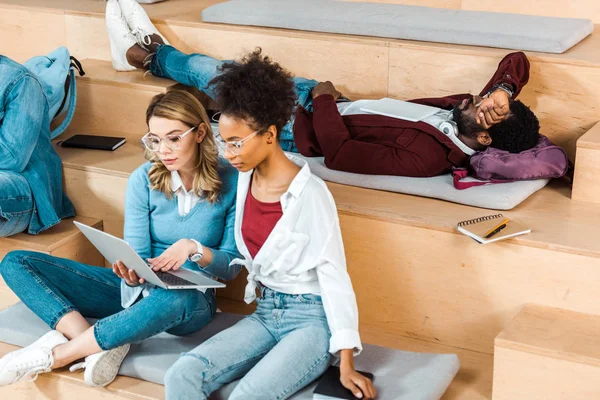 Estudantes multiculturais em óculos usando laptop na sala de aula — Fotografia de Stock