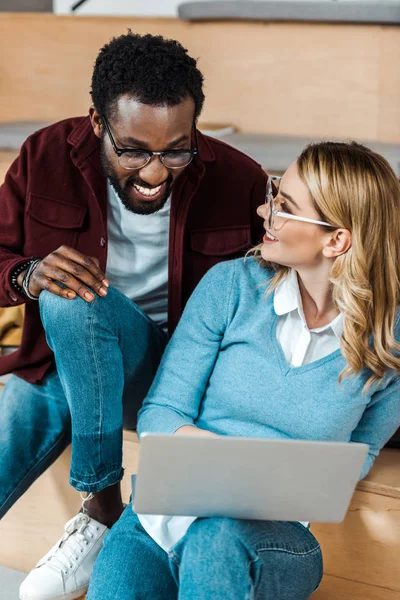 Estudiantes multiculturales sonrientes en gafas usando portátil en la sala de conferencias - foto de stock