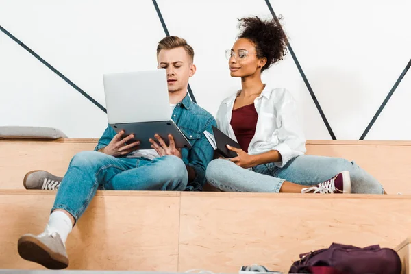 Dos estudiantes multiculturales que utilizan el ordenador portátil en la sala de conferencias - foto de stock