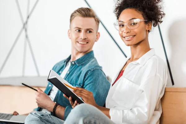 Due studenti multietnici con quaderno in aula magna — Foto stock