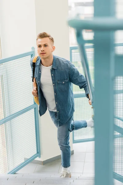 Біг студент в джинсовій сорочці з рюкзаком в коледжі — стокове фото