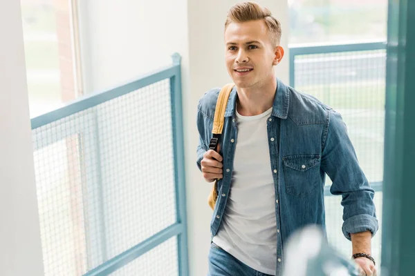 Estudiante sonriente en camisa de mezclilla con mochila en la universidad - foto de stock