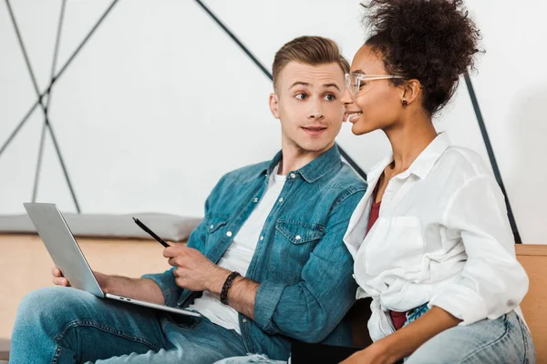 Deux étudiants multiethniques joyeux utilisant un ordinateur portable à l'université — Photo de stock